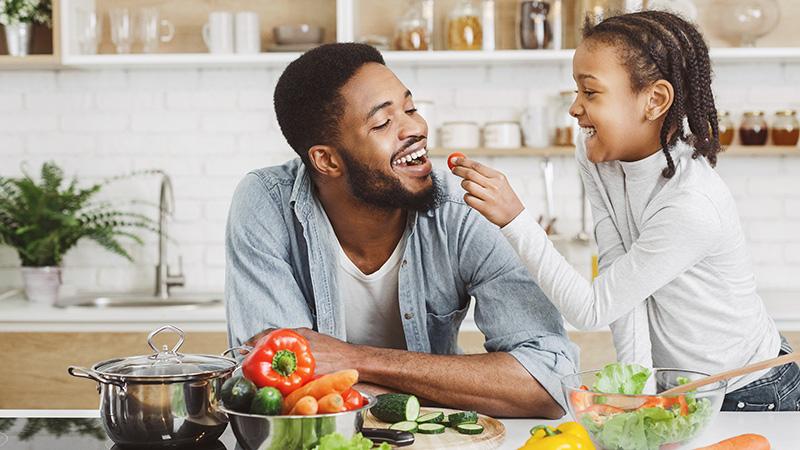 A giggling girl feeding her dad a cherry tomato
