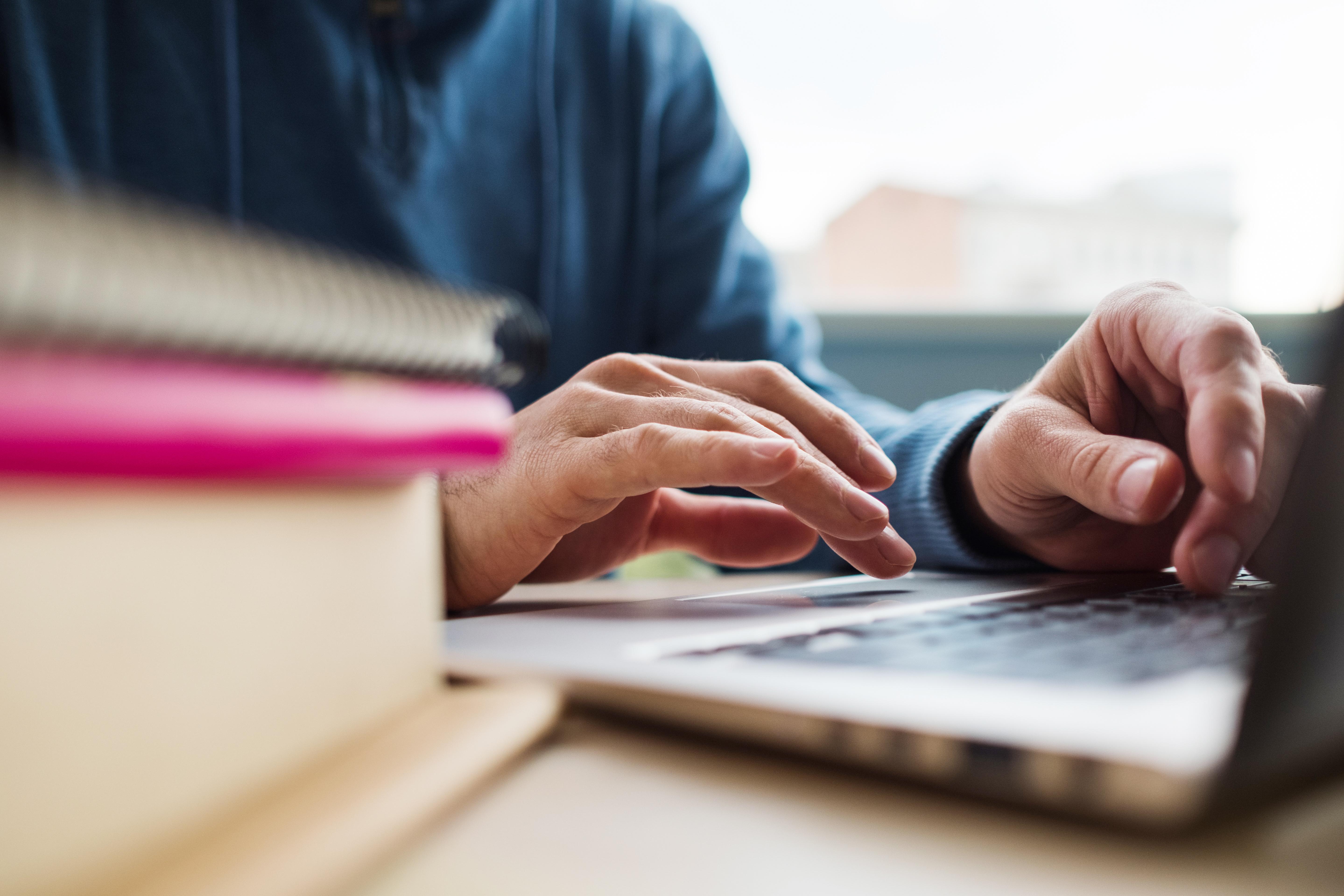 Older man types on laptop next to stack of textbooks