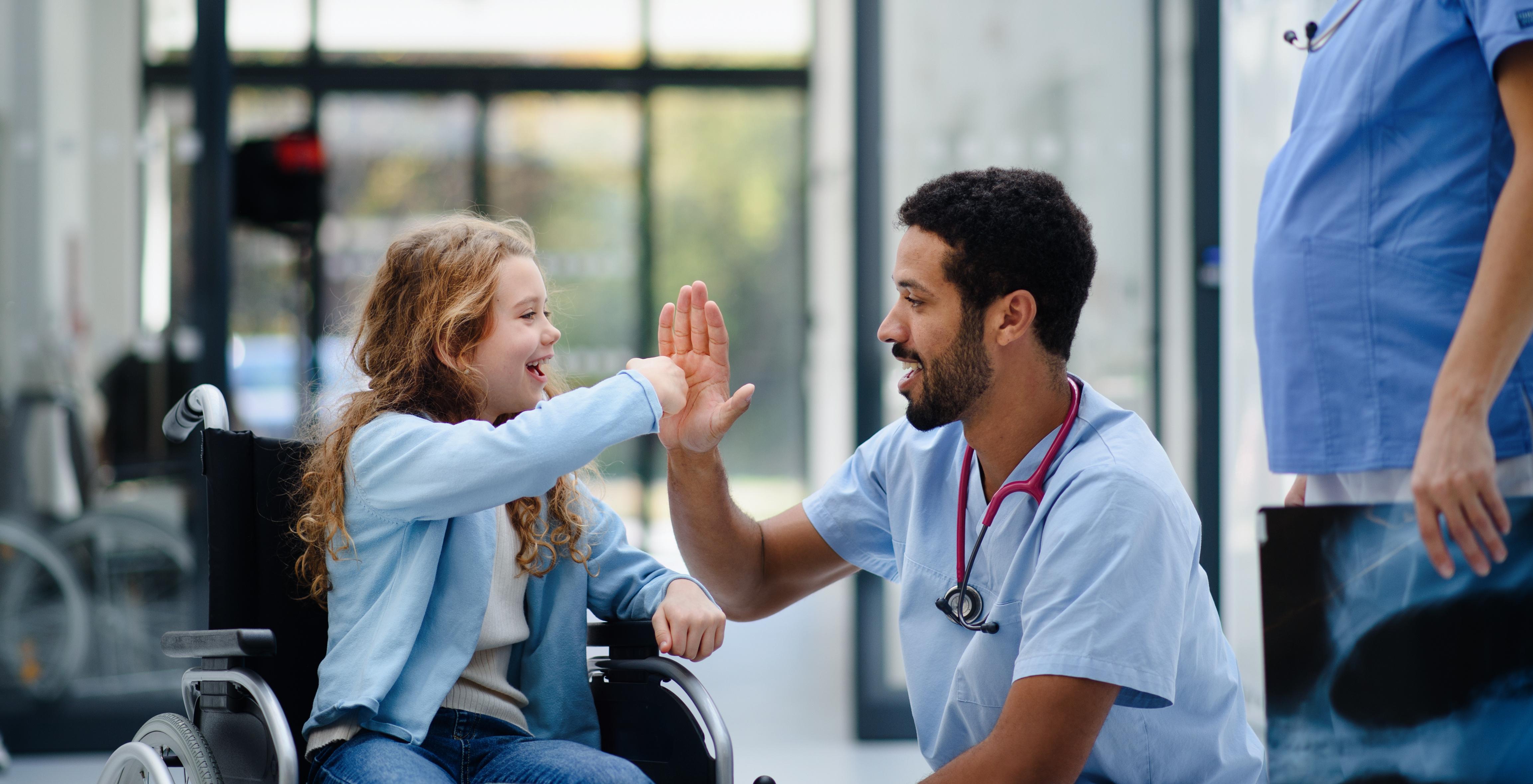 Young doctor high fives child in a wheelchair